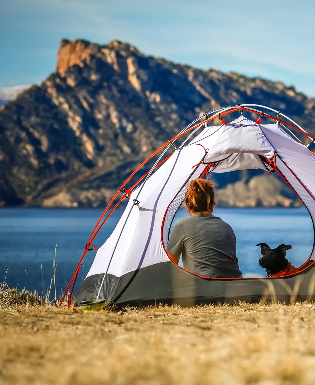 A camper sitting in a tent by a mountain lake, reached by a MOICO walkie talkie